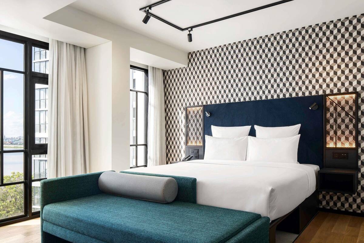 Una habitación de hotel moderna con una cama grande, un sofá, vistas por una ventana y un papel tapiz estampado.