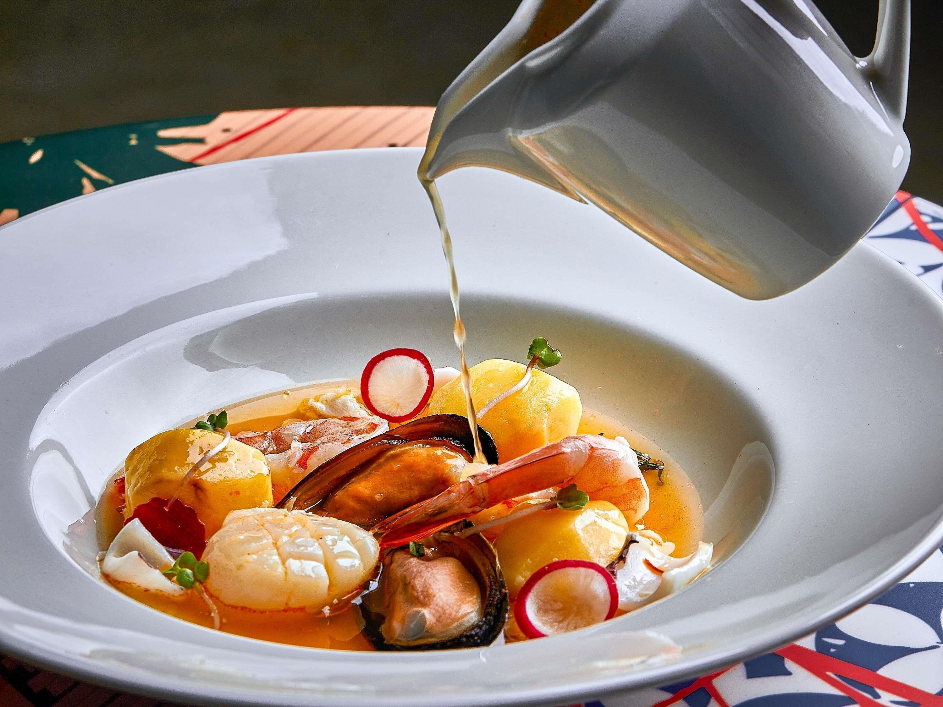 A seafood dish with a pitcher pouring liquid, garnished with radishes and herbs.