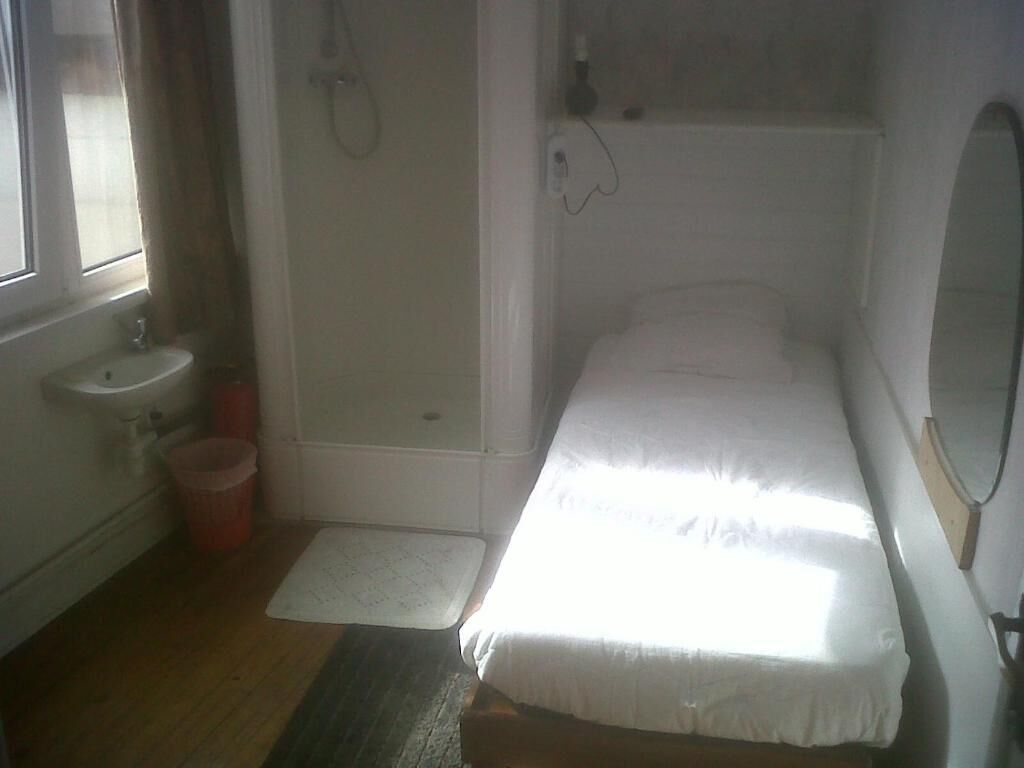 Ein kleines Zimmer mit einem Einzelbett, einem Fenster, einem Waschbecken und einer Dusche.