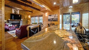 L’intérieur d’un chalet en bois, avec une cheminée, un canapé en cuir, une table à manger et de grandes fenêtres.