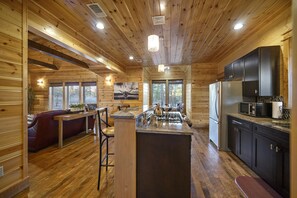 A wooden cabin interior with a kitchen, dining area, and a bar. - Midnight Rhapsody-Romantic Cabin with Large Jacuzzi Tub & Outdoor Gas Fireplace (Broken Bow)