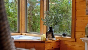 L’intérieur d’une cabane en bois, avec une fenêtre, un petit lavabo, des bougies, une horloge et une plante en pot.