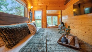L’intérieur d’un chalet en rondins accueillant, avec un lit, un banc en bois et une grande fenêtre donnant sur la forêt.
