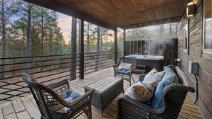 Une terrasse extérieure couverte, aménagée avec des meubles en osier, un jacuzzi et offrant une vue sur une zone boisée.