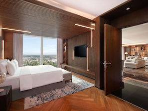 Una habitación de hotel moderna con una cama grande, televisión, zona de estar y vistas a la ciudad.