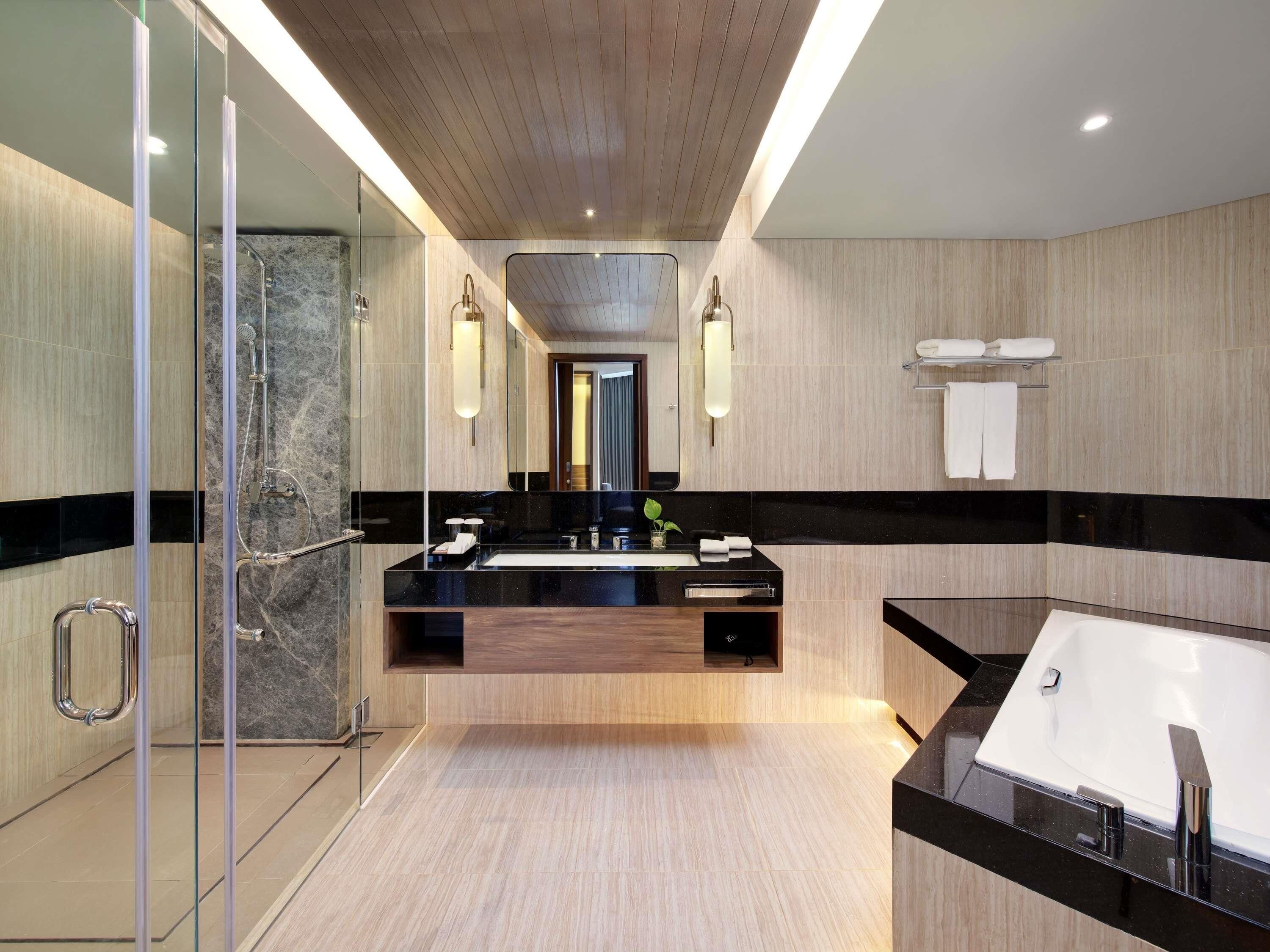 A modern bathroom with a glass shower enclosure, a central sink with a black countertop, and a separate bathtub.