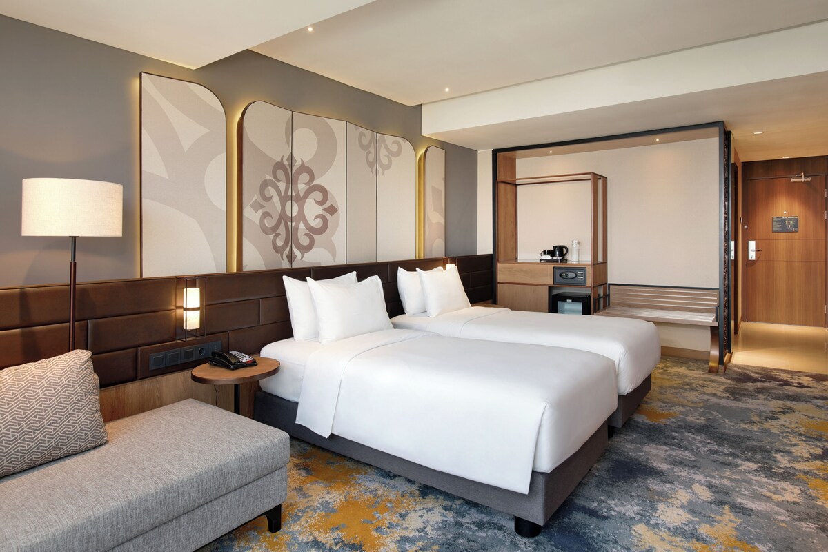 A hotel room with a large bed, a bedside table with a lamp, a sofa, and a mirror.