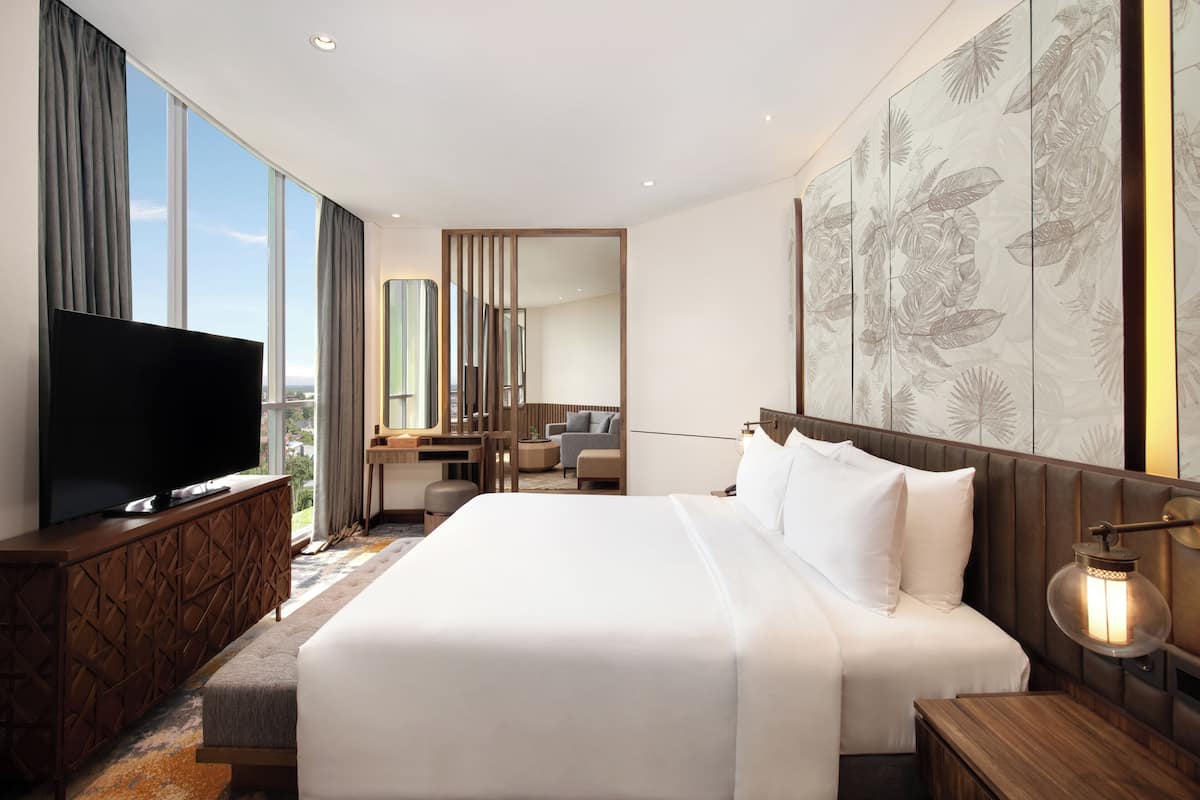 A modern hotel room with a large bed, a flat-screen TV, a desk, and a large window offering a city view.
