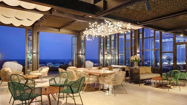 Un espace repas moderne doté de grandes fenêtres, de meubles en osier et d’un lustre original.