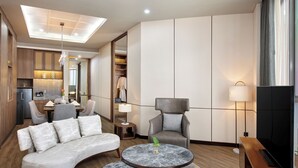 A modern hotel room with a curved sofa, two marble-topped side tables, a grey armchair, a TV, and a large mirror. - Mercure Pangkalan BUN (Pangkalan Bun)