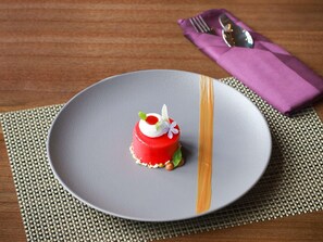 A plate with a red dessert on a grey plate, a purple napkin with a fork and spoon, and a woven placemat. - Mercure Pangkalan BUN (Pangkalan Bun)