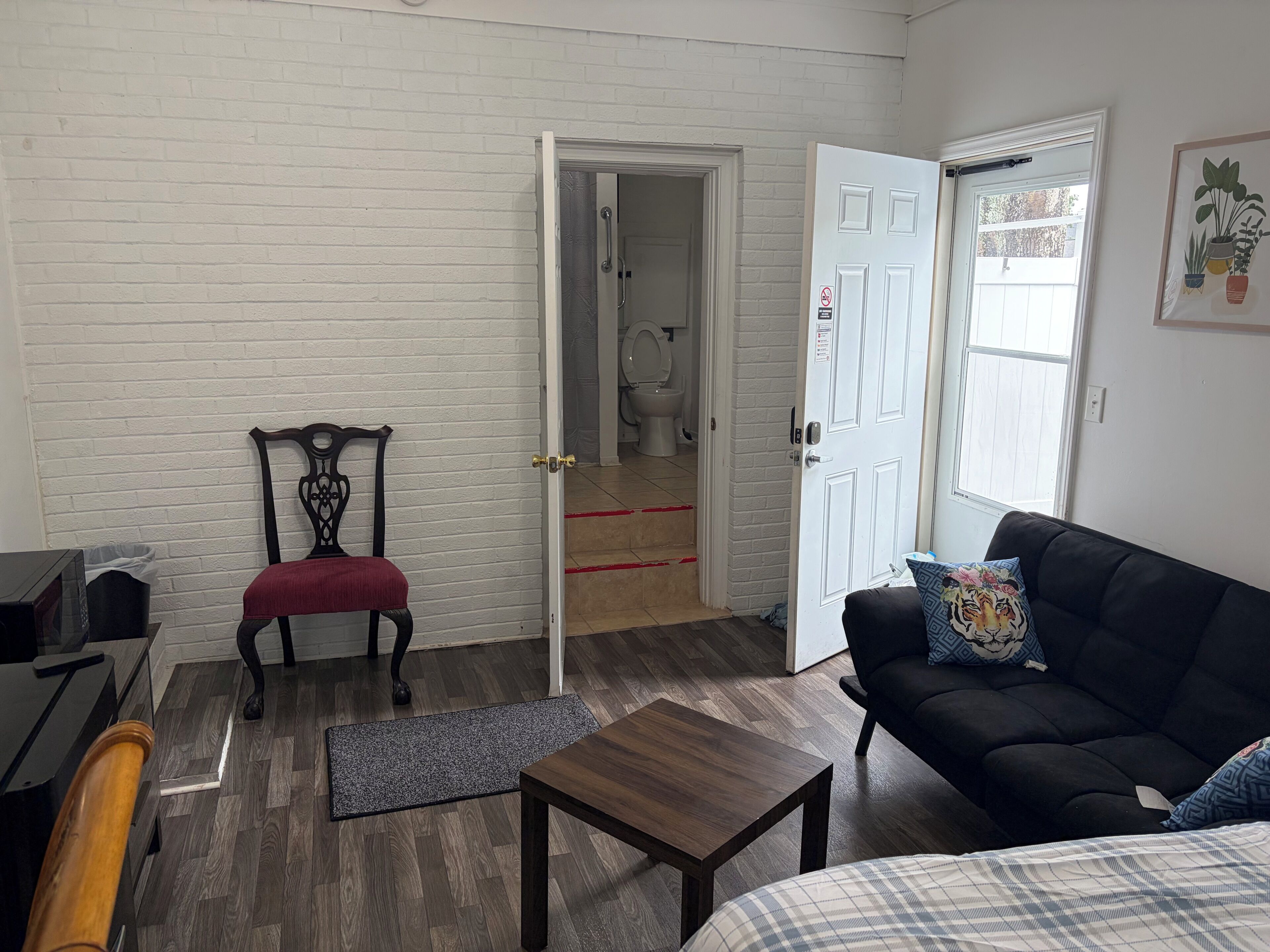 A room with a black sofa, a wooden coffee table, a red cushioned chair, a white door, and a white brick wall.