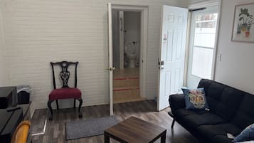 A room with a black sofa, a wooden coffee table, a red cushioned chair, a white door, and a white brick wall.