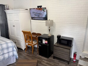 Une chambre d’hôtel équipée d’un lit, d’une armoire, d’une télévision, d’un bureau avec une chaise, d’une machine à café, d’un four à micro-ondes et d’un extincteur.