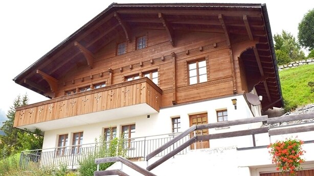 Eine zweistöckige Holzchalet mit Balkon, Steintreppe und Steinmauer.