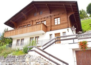 A two-story wooden chalet with a balcony, stone steps, and a stone wall. - 1 Bedroom Apartment in Hasliberg-Wasserwendi (Hasliberg-Wasserwendi)