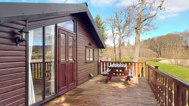 Une terrasse en bois avec une table de pique-nique, des portes vitrées et une rambarde.