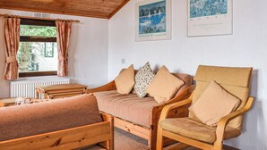 Une pièce chaleureuse avec un plafond en bois, un canapé avec des coussins, une chaise en bois, une petite table et deux tableaux encadrés accrochés au mur.