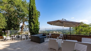 An outdoor patio with wicker furniture, a large umbrella, and a view of the cityscape. - La Corte del Grillo - Residenza d'Epoca (Chiusi)