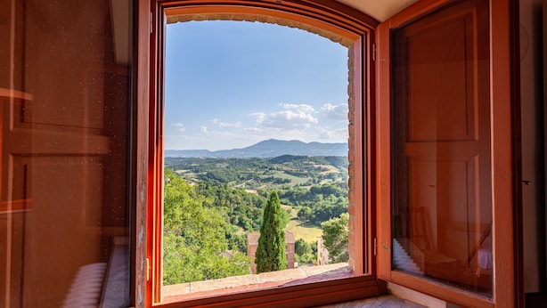 A room with an open window revealing a scenic view of a valley with trees and distant mountains. - La Corte del Grillo - Residenza d'Epoca (Chiusi)