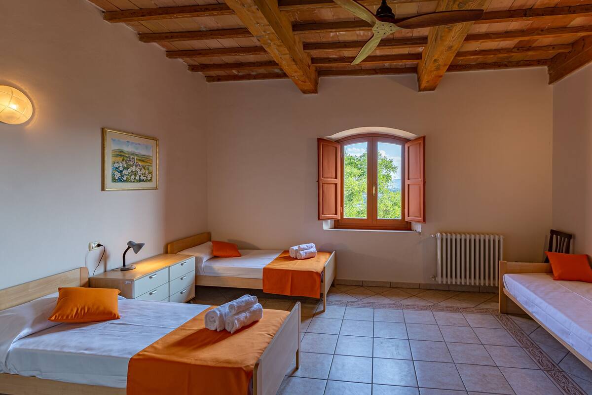 Un dormitorio con dos camas, una mesita de noche, una lámpara, una ventana con contraventanas y un radiador.