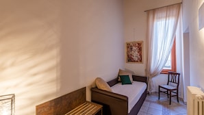 A bedroom with a bed, a chair, a bench, a window with curtains, and a radiator. - La Corte del Grillo - Residenza d'Epoca (Chiusi)