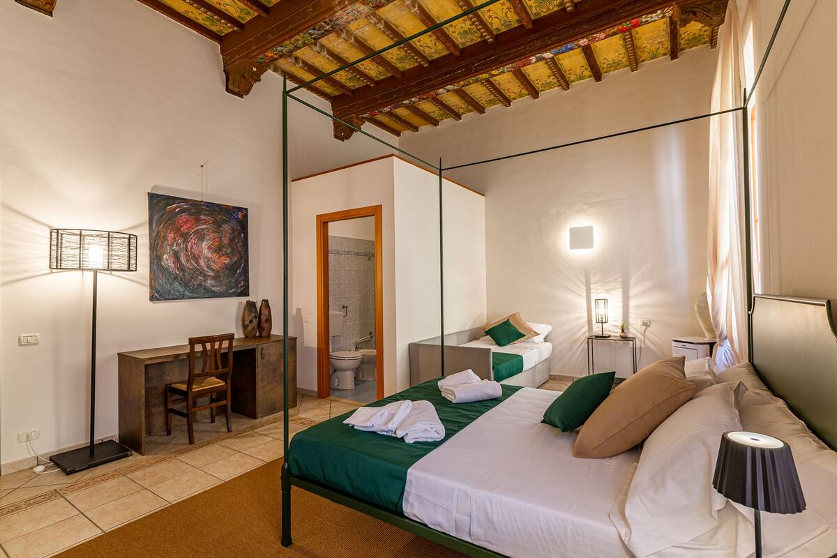 Un dormitorio bien iluminado con cama, mesita de noche, lámpara y escritorio con silla.