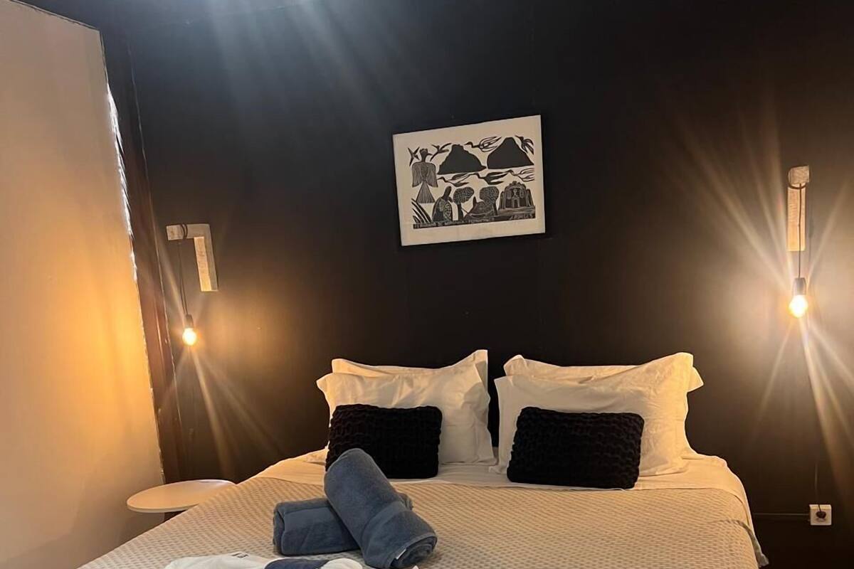 Een opgemaakt bed met een beddekleed met dessin, witte kussens en een donge dekens.