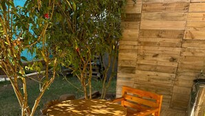 Una terraza de madera con una mesa redonda y dos sillas, rodeada de árboles y un muro de madera.