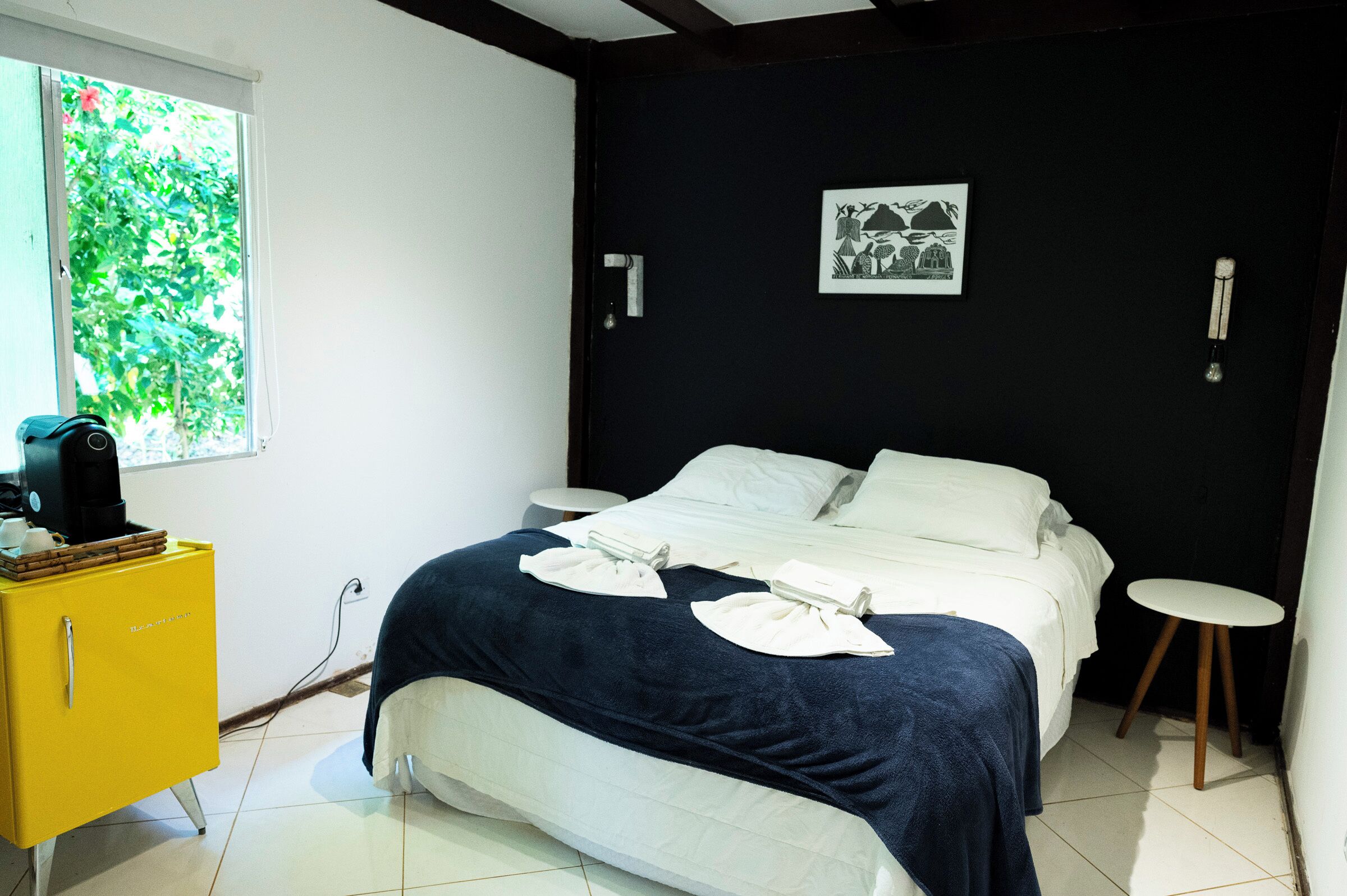 Quarto com uma cama, um armário amarelo, uma janela e um quadro pendurado na parede.