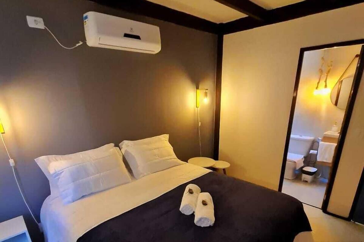 Een hotelkamer met een bed, nachtkastjes, een airconditioner en een spiegel die een badkamer weerspiegelt.