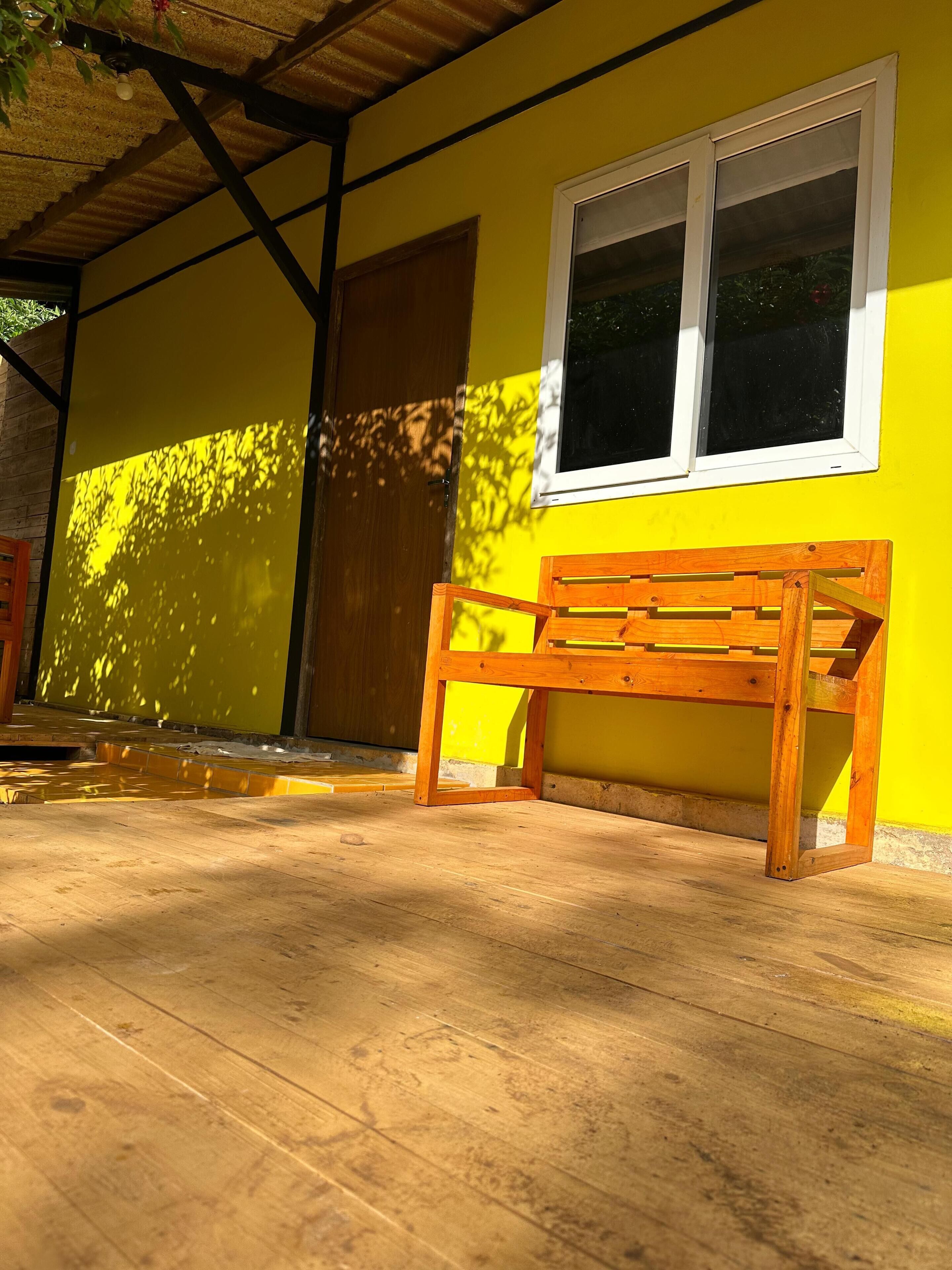 A wooden bench outside a yellow building with a window and a door.