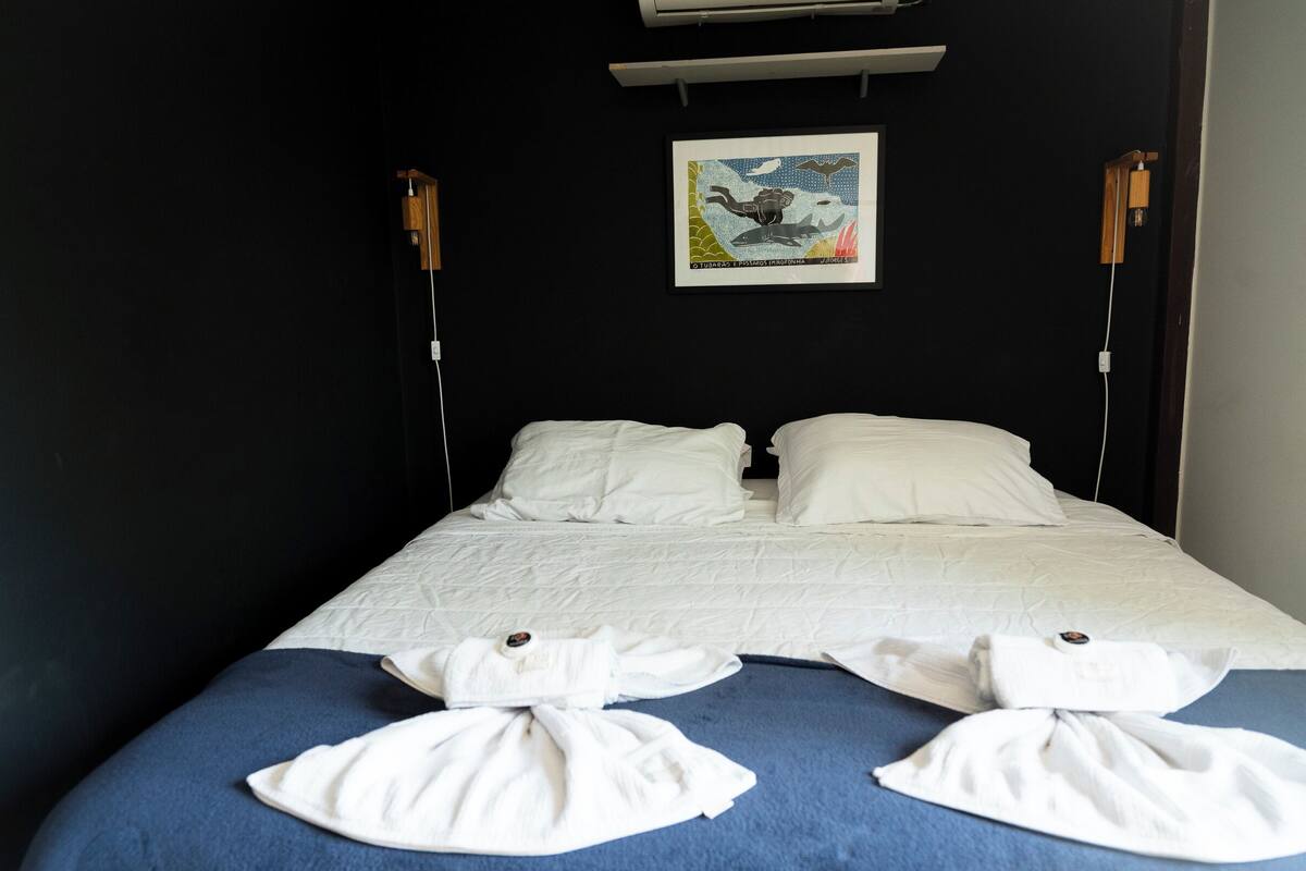 Een hotelkamer met een bed, twee witte kussens, een blauwe deken en twee handdoeken die op het bed zijn gevouwen.