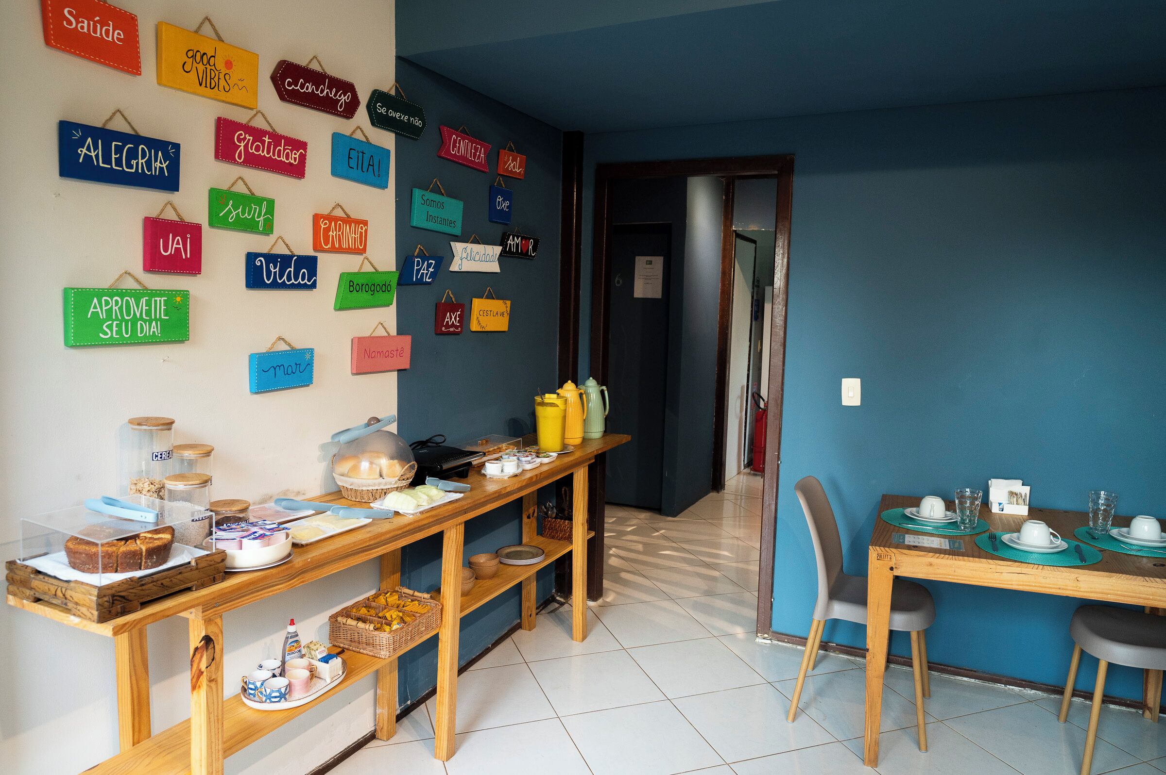 A dining area with a wooden table set for two, a buffet with various food items, and a wall decorated with colorful signs in multiple languages.