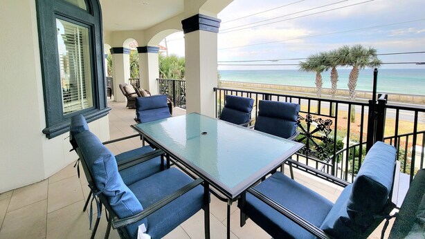 A balcony with a table and chairs, overlooking a beach with palm trees and the ocean. - Front Row Beach House 6BR/5.5 bath private pool and private beach access. (Miramar Beach)