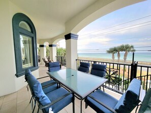 Ein Balkon mit Tisch und Stühlen, der auf einen Strand mit Palmen und das Meer blickt.