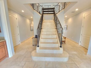 Stunning staircase with a black railing, flanked by doors and a wicker chair.