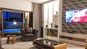 A modern living room with a leather sofa, a glass coffee table, and a flat-screen TV mounted on a stone-textured wall. - Stay.Plus Diani Luxurious Villa (Diani Beach)