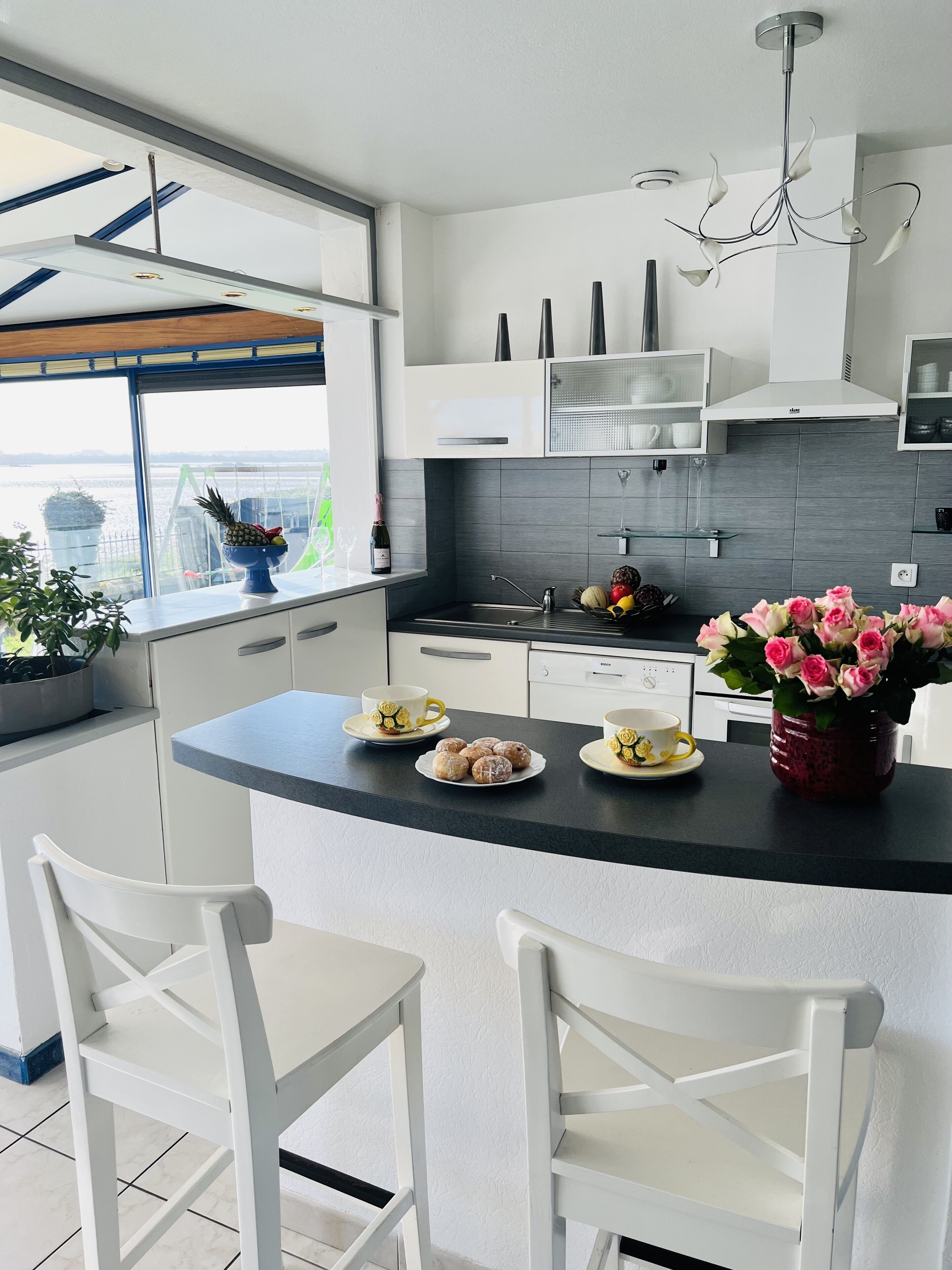 A modern kitchen with a central island, white cabinetry, and a view of a body of water through a large window.