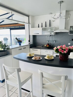 A modern kitchen with a central island, white cabinetry, and a view of a body of water through a large window.