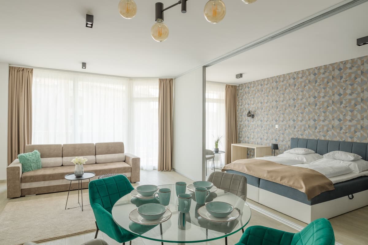 Ein modernes Hotelzimmer mit Bett, Sofa, Esstisch und Glastisch.