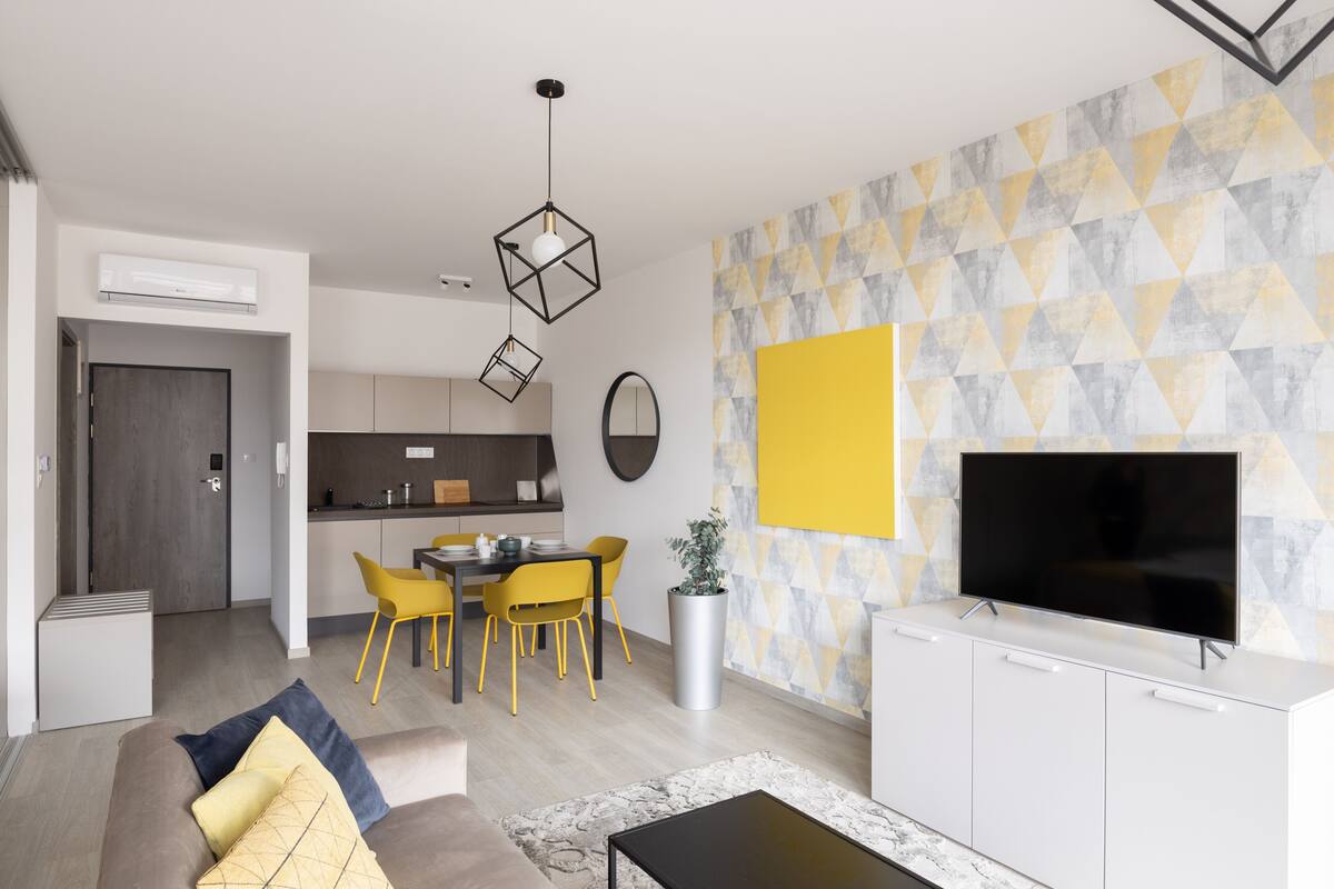 Ein modernes Wohnzimmer mit einer Couch, einem Couchtisch und einem Fernseher auf einem Schrank. Es gibt einen Essbereich mit Tisch und Stühlen.
