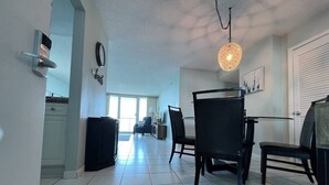 A spacious living area with a dining table, chairs, a black cabinet, a wall clock, and a hanging light fixture. - Wake up with a view in a beautiful condo (Pensacola Beach)