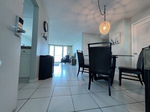 Amplia sala de estar con una mesa de comedor, sillas, un armario negro, un reloj de pared y una lámpara colgante.