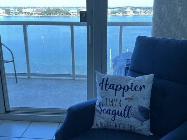 Un balcón con vista al agua, una silla con cojín y una ventana con vista al agua.
