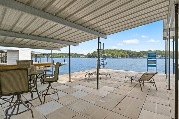 Relax by the serene water's edge, where a patio offers a table, chairs, bar, and lounge seating under a sheltered roof.