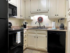 Kitchen area with refrigerator, microwave, and dishwasher, featuring white cabinetry and a stainless steel sink.