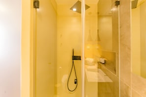 A glass-enclosed shower with a handheld showerhead, a towel, and toiletries on a shelf.