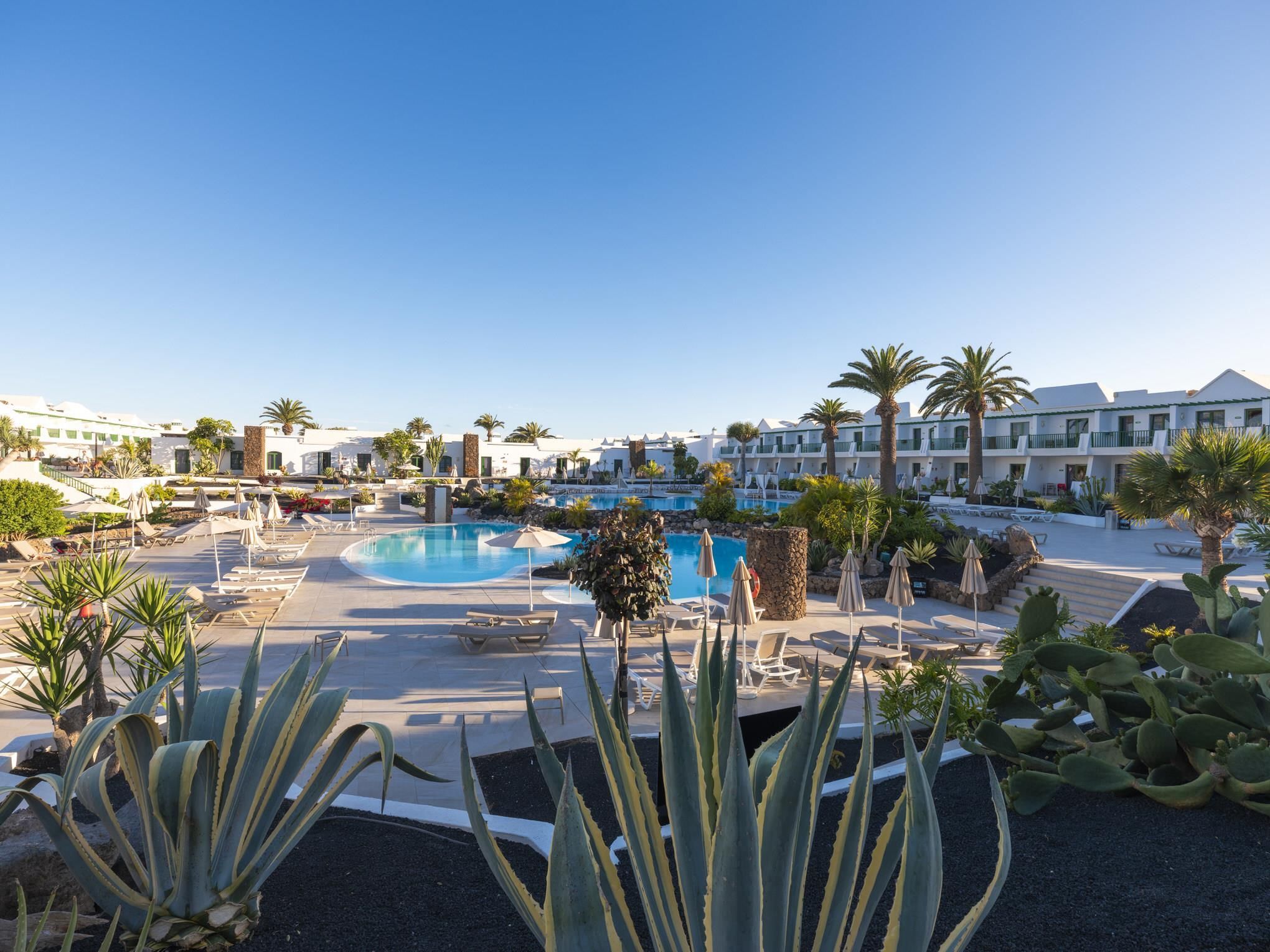Un complexe hôtelier doté de plusieurs piscines, de palmiers et de chaises longues.