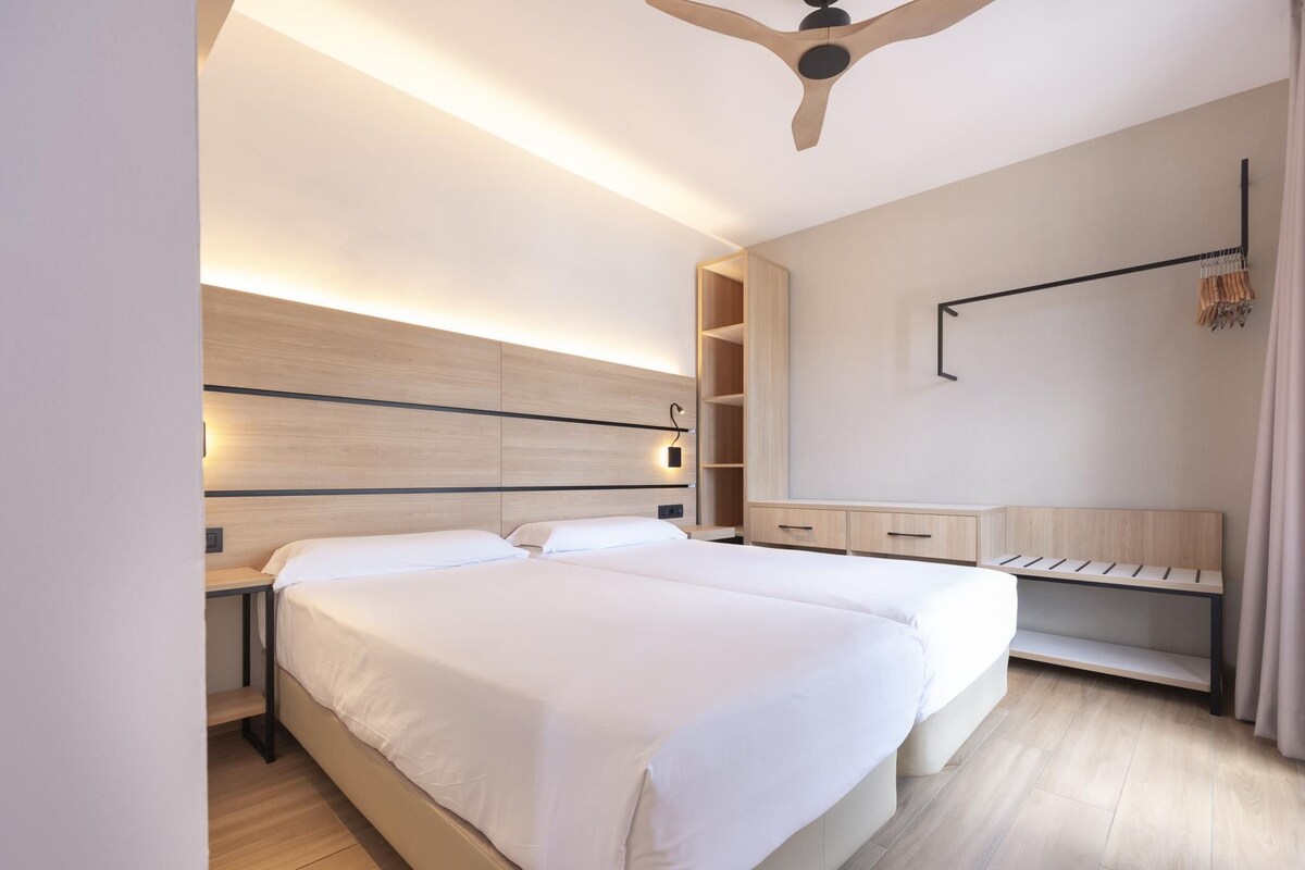 A modern hotel room with a large bed, bedside tables, a desk, and a ceiling fan.